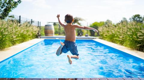 Un jeune garçon en maillot de bain saute dans une belle piscine privative bordée de plantes
