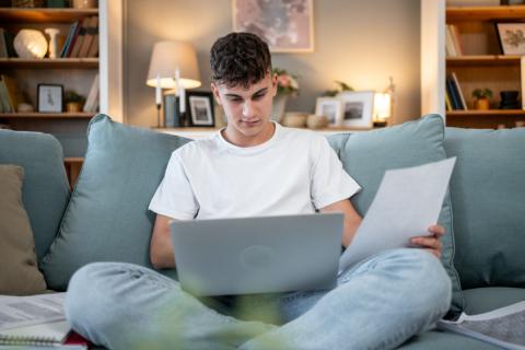 Un étudiant travaille sur son ordinateur sur le canapé bleu clair du salon.
