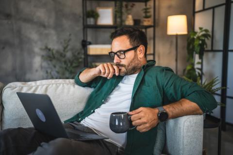 Homme assis sur son canapé, avec son mug et son ordinateur.