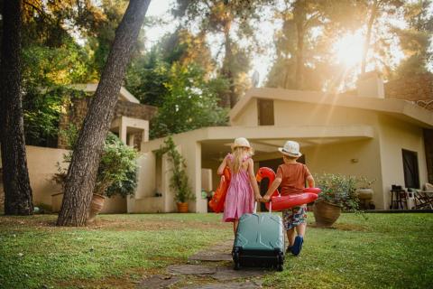 jeunes enfant traversent avec valise et bouées le jardin de la location de vacances