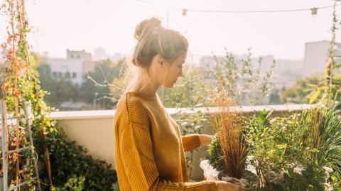 Une jeune femme portant ses cheveux relevés en chignon s'occupe de ses plantes vertes sur son balcon