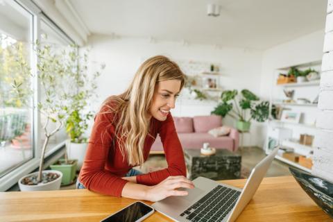 Femme avec un pull rouge sur son ordinateur dans son salon lumineux. 