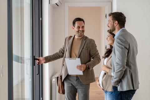 Un couple visitant un bien immobilier avec un agent en veste marron. 
