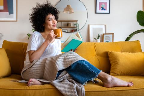 Femme afro américaine souriante, avec un mug sur son canapé jaune moutarde. 