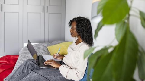 Une jeune femme fait des recherches sur son pc portable, assise sur son canapé