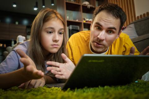 Un père et sa fille adolescente regardent un écran d'ordinateur, allongés à terre. 