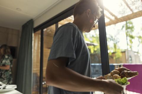 Jeune homme qui sert les croissants dans un mobil-home de vacances. 