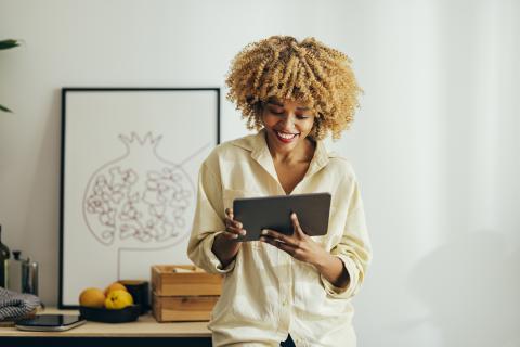 Afro-American Woman Standing and Smiling While Looking at a Digital Tablet