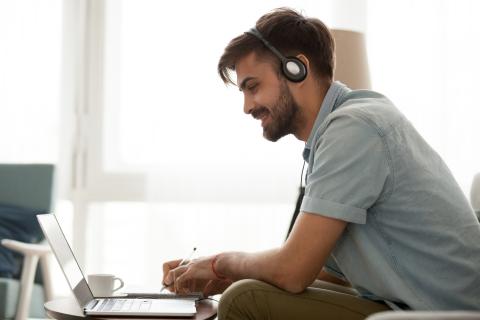 Happy man wearing headset study online on laptop making notes