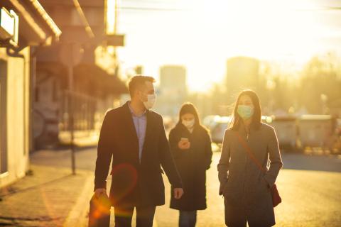 Two diverse coworkers walking and chatting. Two colleagues wearing pollution masks. Going to a job.