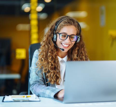 Femme souriante au travail avec un ordinateur et un casque. 
