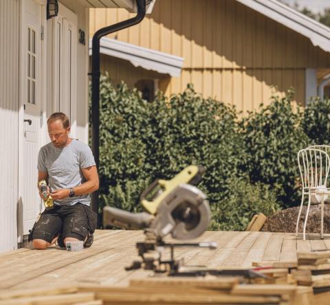 Un homme est en pleine construction d'une terrasse en bois, accolée à sa maison