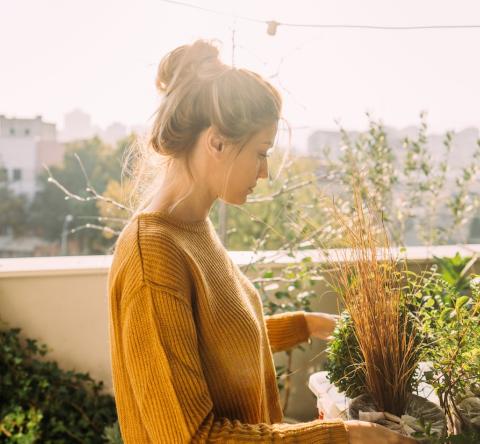 Une jeune femme portant ses cheveux relevés en chignon s'occupe de ses plantes vertes sur son balcon