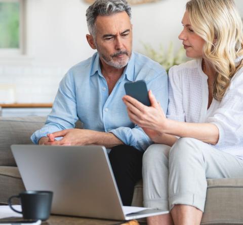 Femme sur le canapé montre à son époux son téléphone où il peut lire des infos sur la trêve hivernale