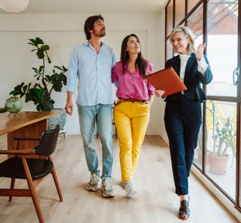 Un agent immobilier femme fait visiter un beau logement lumineux à un couple. 
