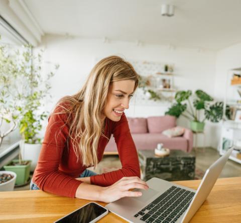 Femme avec un pull rouge sur son ordinateur dans son salon lumineux. 