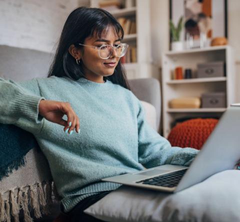 jeune femme assise près de son canapé regarde son ordinateur