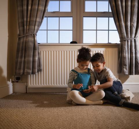 Deux enfants jouent dans une chambre devant un radiateur. 