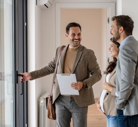 Un couple visitant un bien immobilier avec un agent en veste marron. 