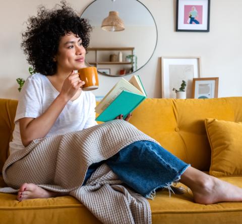 Femme afro américaine souriante, avec un mug sur son canapé jaune moutarde. 