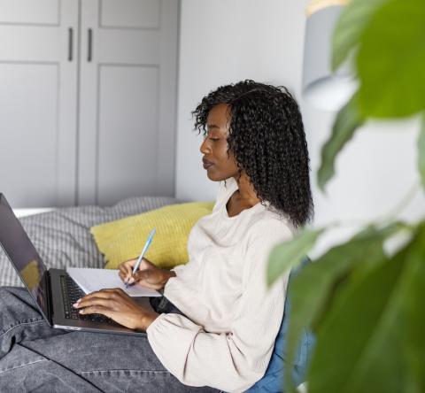 Une jeune femme fait des recherches sur son pc portable, assise sur son canapé