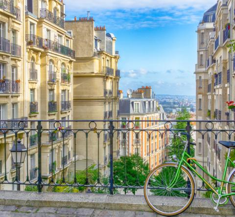 Vélo attaché à un grillage en hauteur, avec vue imprenable sur Paris et ciel bleu. 
