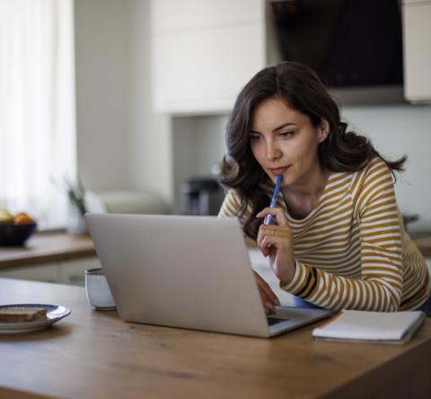 Femme avec marinière jaune et blanche recherchant une information sur son ordinateur, dans la cuisine. 
