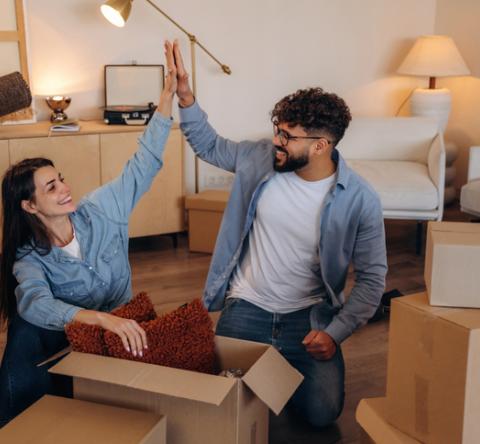 Couple qui se tape dans la main, dans son nouveau salon, entouré de cartons.